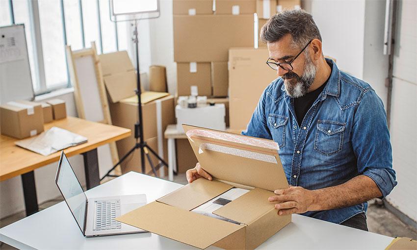 Man staat aan inpaktafel en bereidt een doos voor op een e-commerce verzending