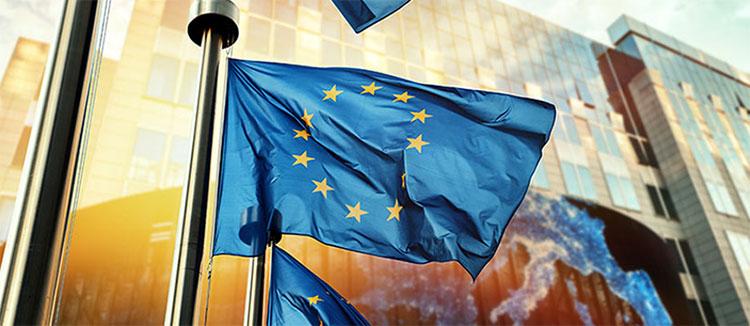 3 drapeaux européens flottent au vent, juste devant un bâtiment