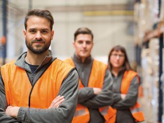 Werknemers met veiligheidsvestje in een magazijn staan in een rij