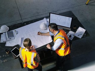 Un homme et une femme se tiennent près d'une table et examinent des plans de construction