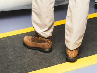 Un homme avec des bottes de travail marron se tient debout sur un tapis anti-fatigue