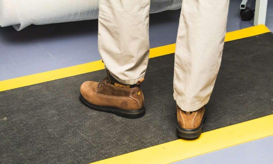 Un homme avec des bottes de travail marron se tient debout sur un tapis anti-fatigue